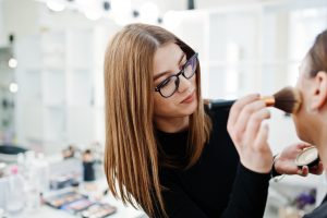 A makeup professional is applying a brush on a customer